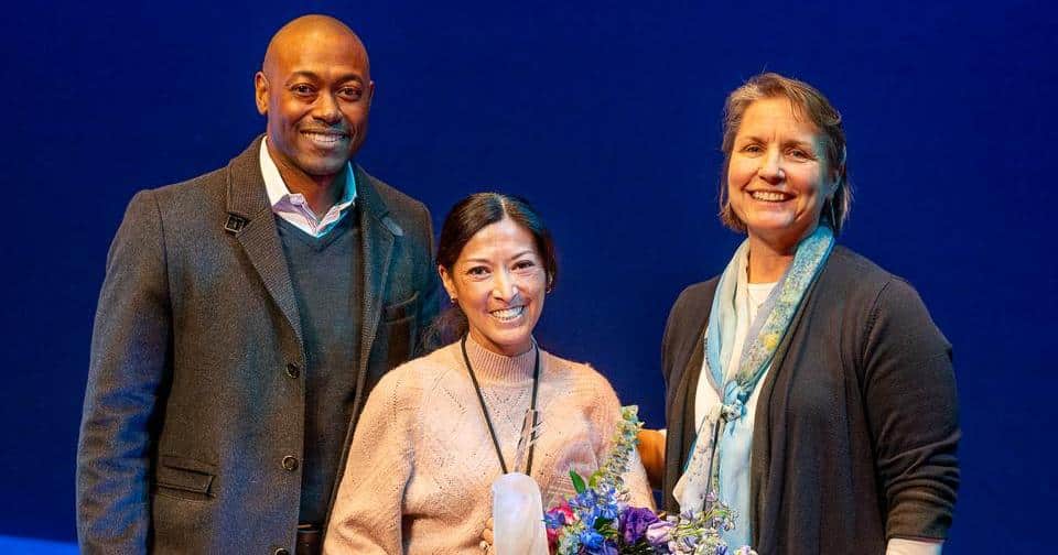 Liz McNeil AwardLiz McNeil Award Three people standing on stage, one holding an award and flowers