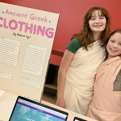 Two smiling students stand next to a poster board