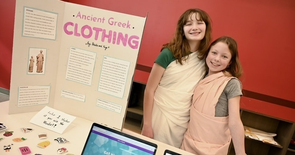 Greek Symposium Class II Two smiling students stand next to a poster board