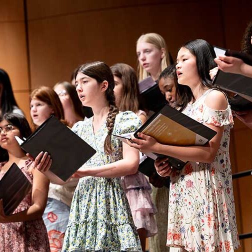 diverse group of girls in spring floral dresses singing on stage