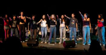 Band members standing on stage hold arm out to audience