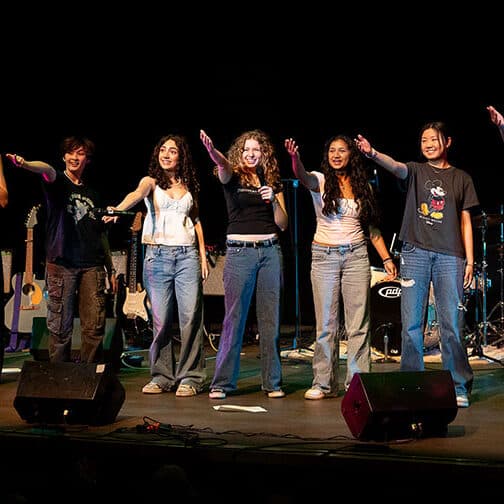 Band members standing on stage hold arm out to audience