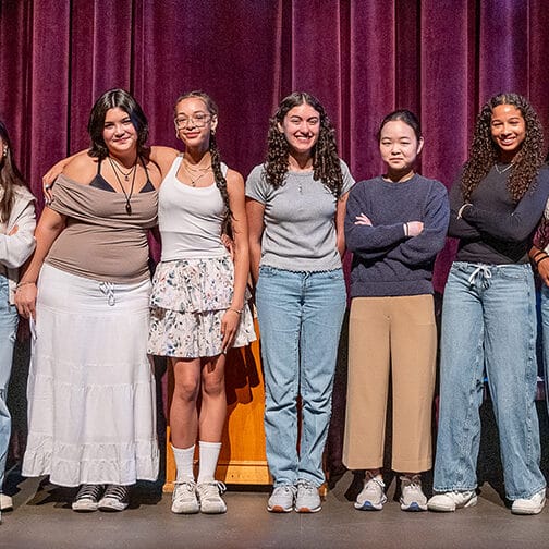9 students stand shoulder to shoulder on stage