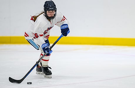 female ice hockey player in white jersey skating on ice with stick and puck