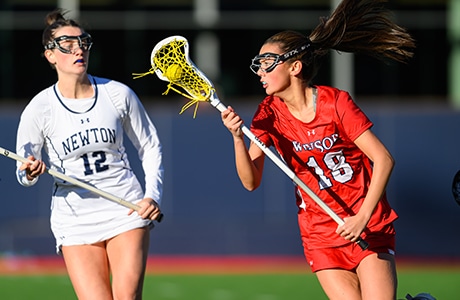 two girls playing lacrosse, one wearing whtie and one wearing red