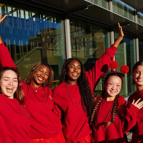 Five students wear red clothing and hold their arms in the air