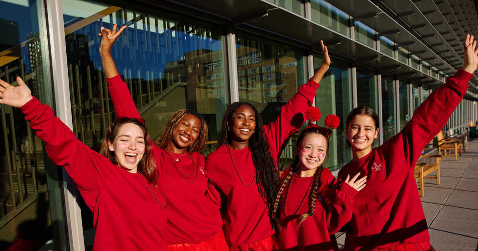 Five students wear red clothing and hold their arms in the air