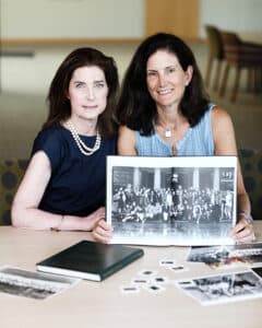 two women holding yearbook showing class photo