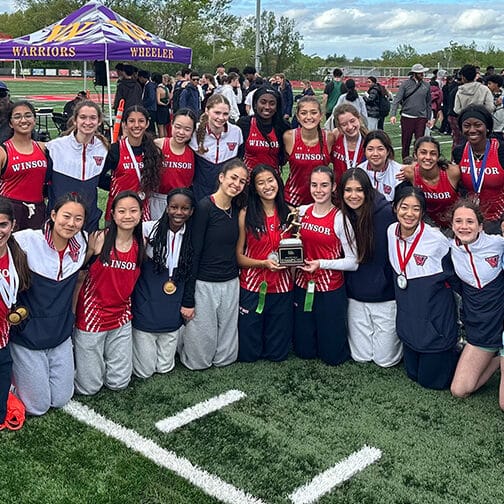 Team of female athletes pose with their first place trophy.