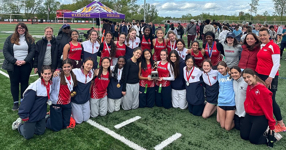 Team of female athletes pose with their first place trophy.