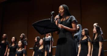 a young woman soloist leads a chorus on stage
