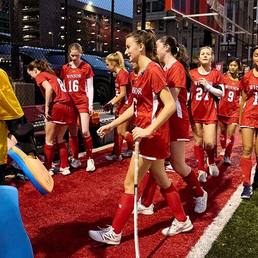 a group of field hockey players on the sideline at night