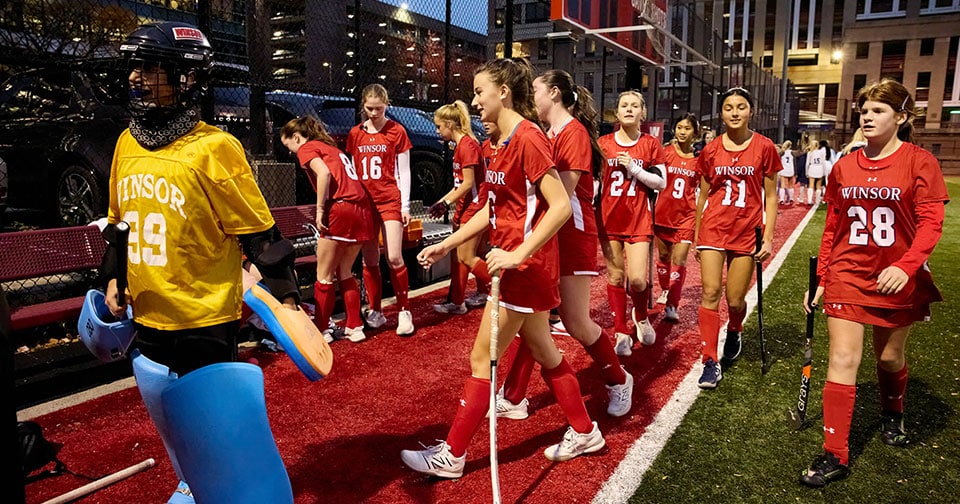 a group of field hockey players on the sideline at night