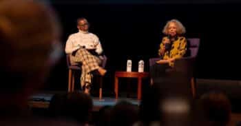 Two women of color seated on a stage holding microphones.