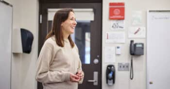 woman with dark hair and a beige sweater in front of a classroom