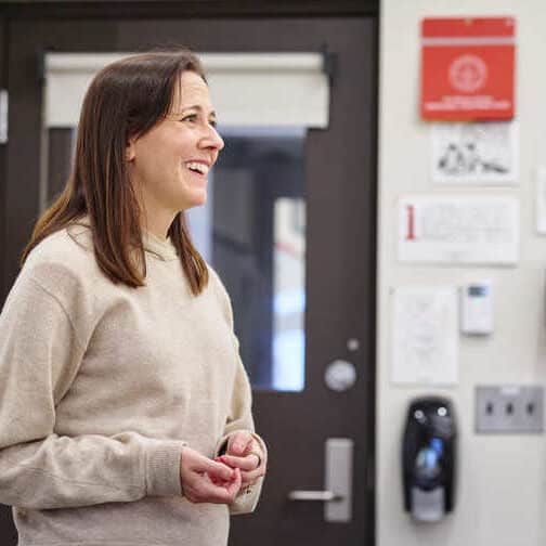 woman with dark hair and a beige sweater in front of a classroom