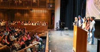 student speakers onstage addressing an auditorium audience