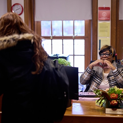 older woman of color making a heart out of hands for a younger student