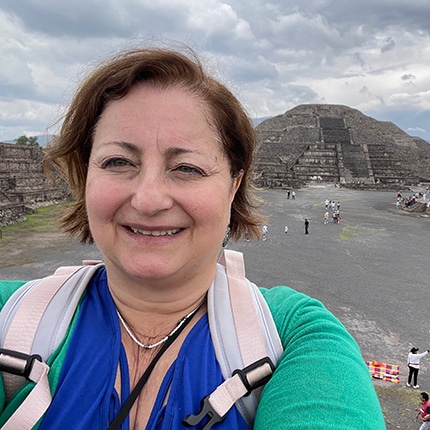Woman wearing green coat taking a selfie in front of pyramids in Mexico