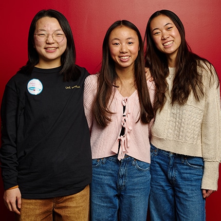 Three female students standing together against a red wall