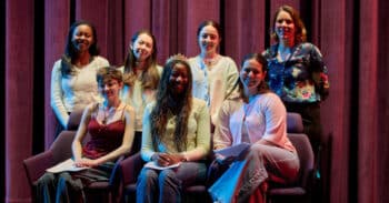 Six young women and the current head of school on stage, smiling