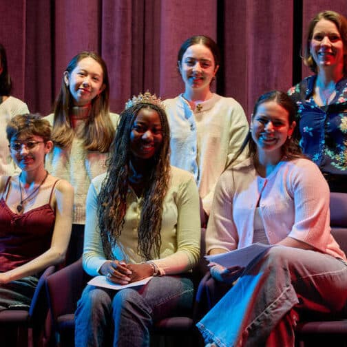 Six young women and the current head of school on stage, smiling