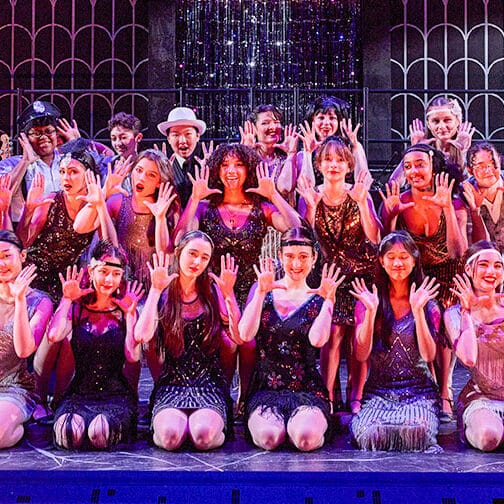 the cast of Chicago poses in a group photo onstage