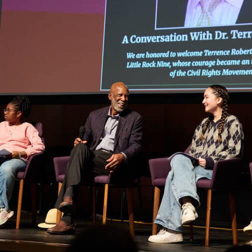 Four students and an adult male seated on a stage