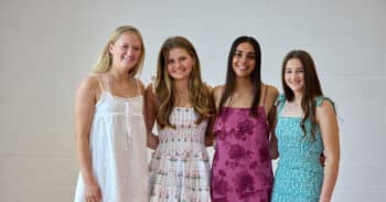 Four young women in sundresses, each with long hair, smiling