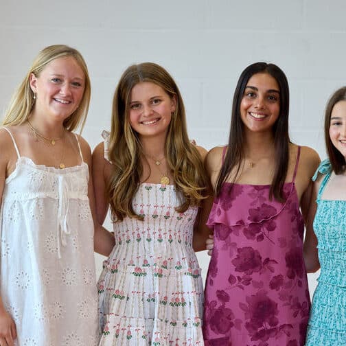 Four young women in sundresses, each with long hair, smiling
