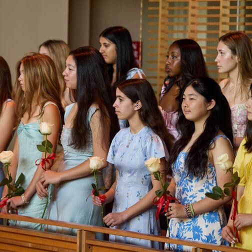 eighth graders in an audience holding white roses