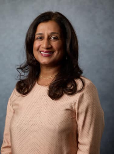 Woman with long, dark hair, smiling and wearing a peach long-sleeved top