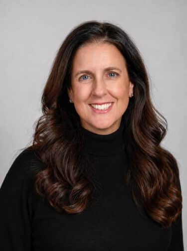 Woman with long, dark hair, smiling and wearing a dark turtleneck top