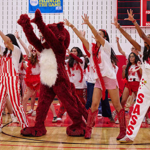A group of students stretch their arms in the air mid dance routine.