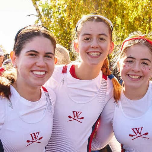 Students wear rowing uni and stand on the dock.