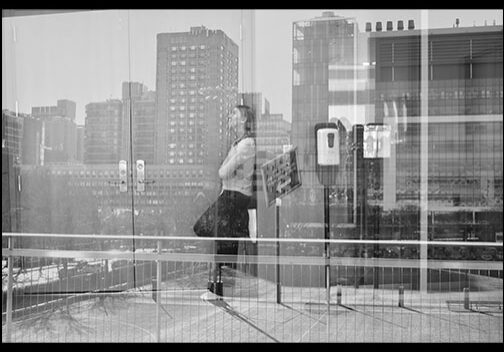 black and white photo of reflection of a woman resting on a wall and buildings behind
